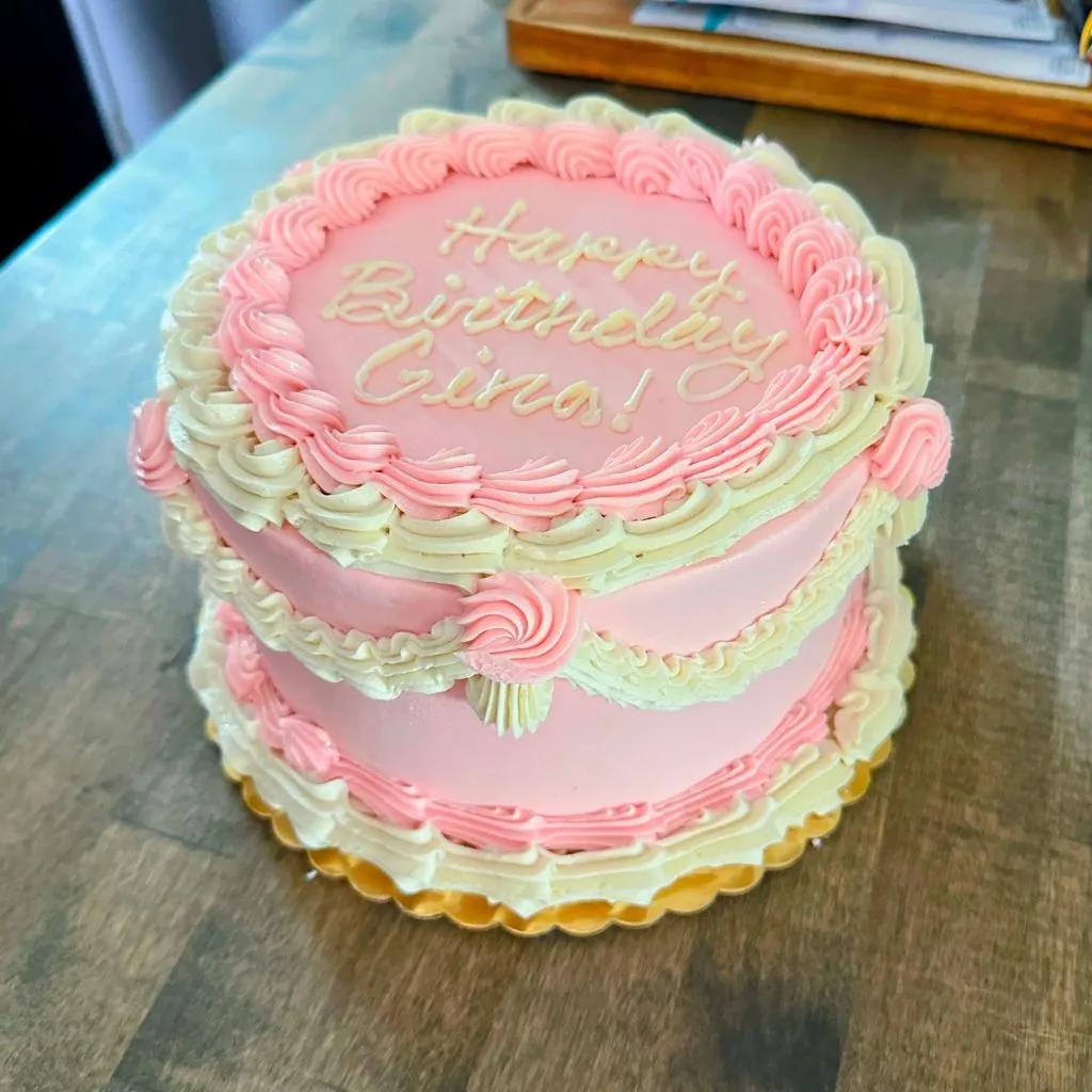 a pink cake with ruffled piping in vintage style with "happy birthday gina" written on it